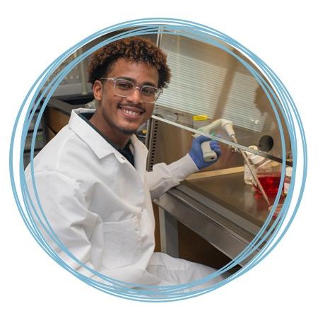 A student wears a white coat as they work in a lab setting for U N E research