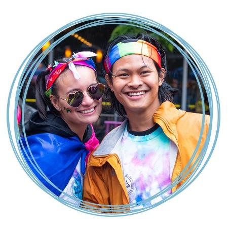 Two U N E students wearing rainbow headbands and smile at a Portland Pride Parade